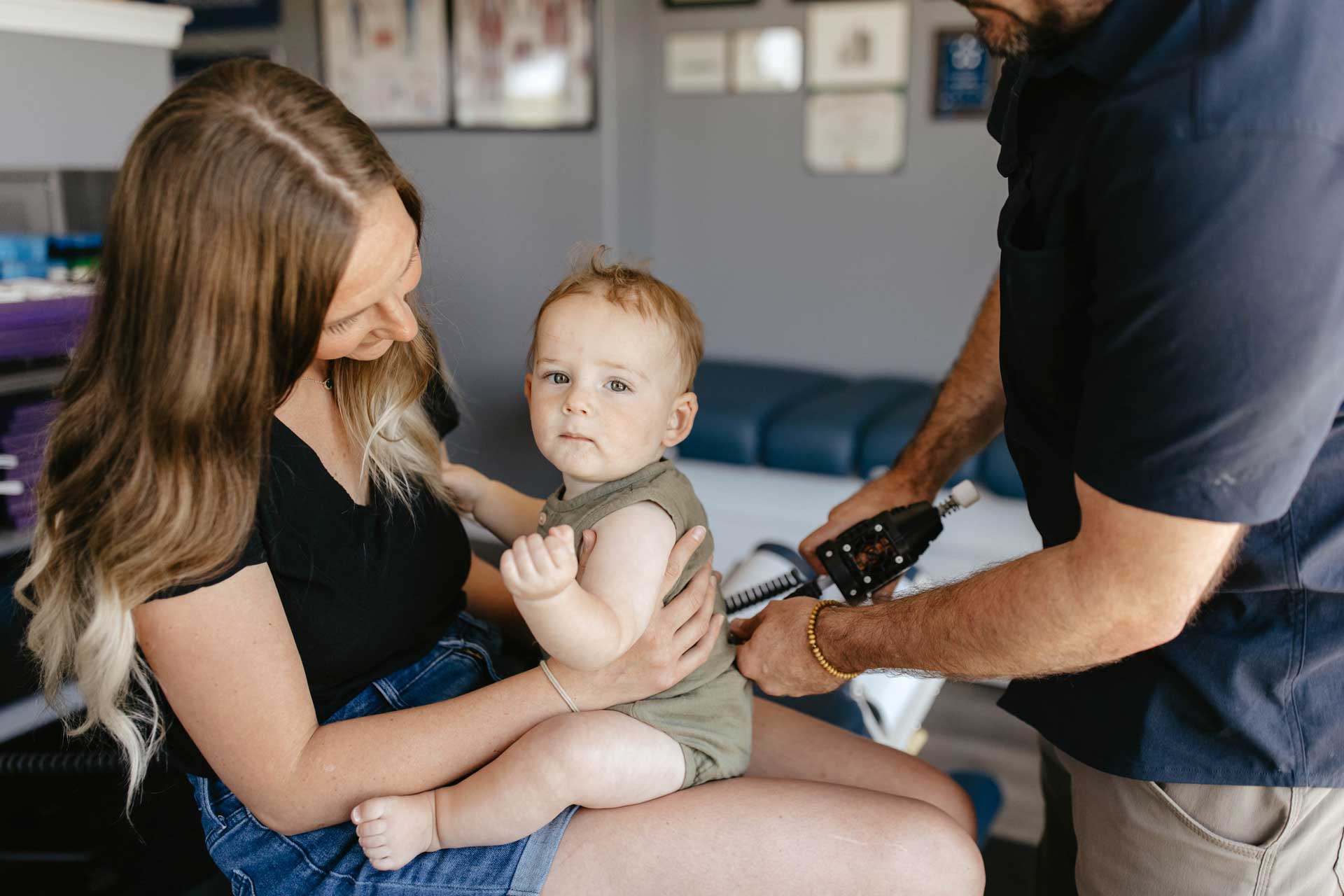 Dr. Miller gently adjusting a 2-year-old child while the mother provides comfort during the chiropractic session.