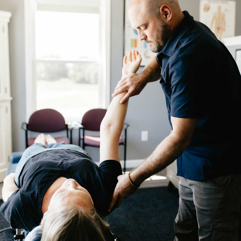 Dr. Dylan Miller performing a muscle test on a patient’s shoulder to assess strength and identify imbalances.